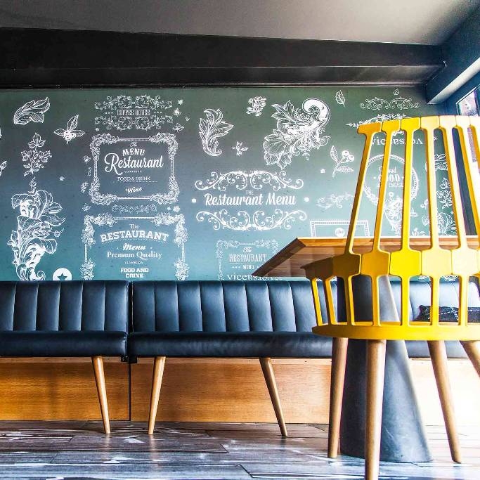 Salle de restaurant moderne avec banquette noire, chaises jaunes et mur décoratif bleu-gris